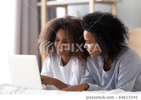 African mom and teen daughter using laptop lying on bed African mom and teen daughter using laptop lying on bed 64613345