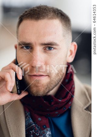 Young serious man wearing scarf and coat talking on mobile phone close-up. Young serious man wearing scarf and coat talking on mobile phone close-up. 64614353