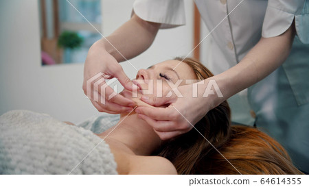 Massage - woman massage therapist massaging the face of a red-haired woman with her hands 64614355