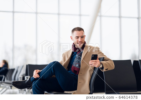 young busy man waiting for departure at the airport while using his phone young busy man waiting for departure at the airport while using his phone 64614378