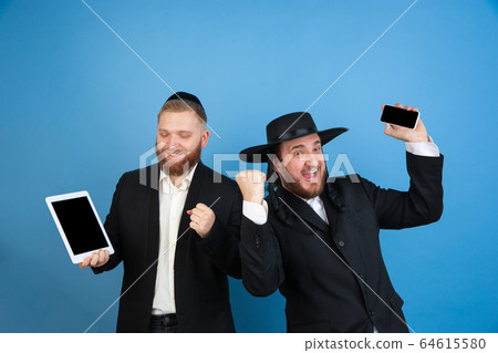Portrait of a young orthodox jewish men isolated on blue studio background, meeting the Passover, winners Portrait of a young orthodox jewish men isolated on blue studio background, meeting the Passover, winners 64615580