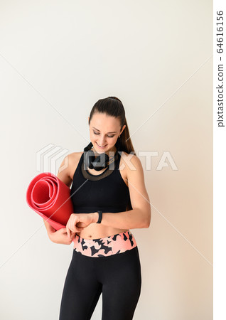 Sporty woman with headphones and rolled mat 64616156