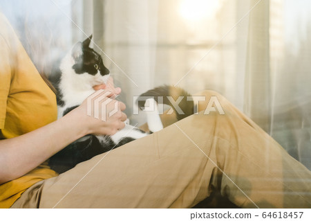 Sad girl in medical protective mask and yellow t-shirt sitting on the windowsill with a black and white Tuxedo cat during a pandemic quarantine coronavirus Covid-19. Isolation at home. Sad girl in medical protective mask and yellow t-shirt sitting on the windowsill with a black and white Tuxedo cat during a pandemic quarantine coronavirus Covid-19. Isolation at home. 64618457