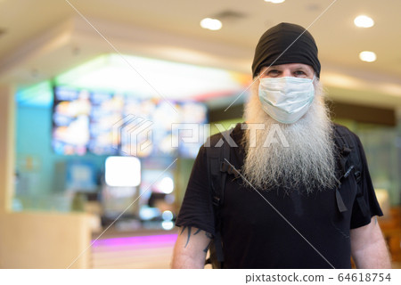 Mature bearded hipster man as backpacker wearing mask inside the mall 64618754