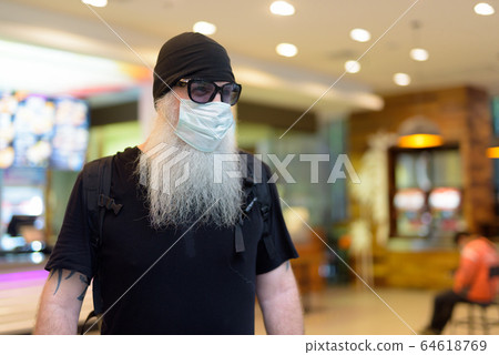 Mature bearded hipster man as backpacker with mask and sunglasses thinking at the mall 64618769