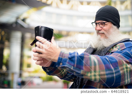 Mature handsome bearded man taking selfie in the city outdoors 64618921