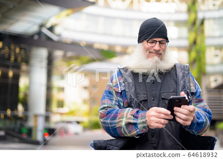 Mature handsome bearded man using phone in the city outdoors Mature handsome bearded man using phone in the city outdoors 64618932