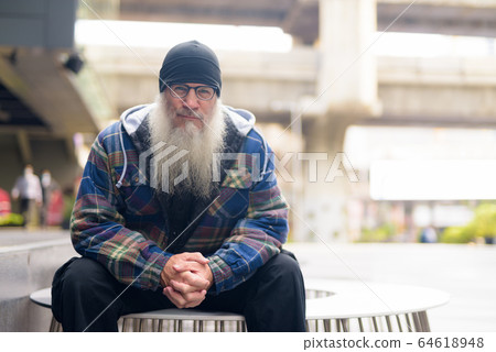 Mature bearded hipster man with eyeglasses sitting in the city outdoors Mature bearded hipster man with eyeglasses sitting in the city outdoors 64618948