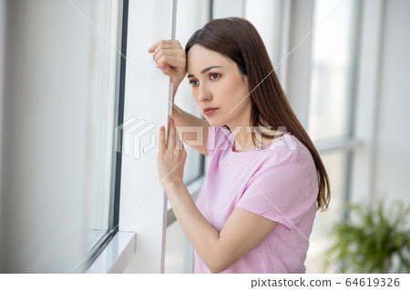 Young sad woman standing near the window. 64619326