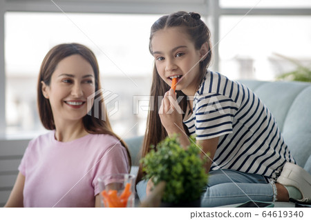 Mom looking at her daughter eating a carrot. 64619340