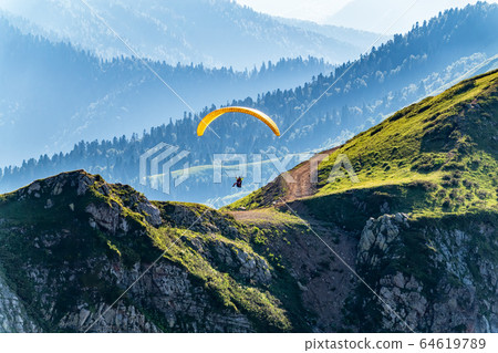 Yellow paraglider fly over mountain slope on sunny day 64619789