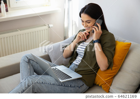 Cheerful pretty lady using laptop and having phone conversation 64621169