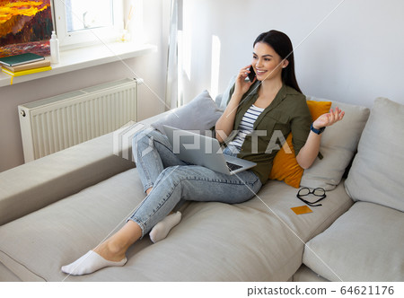 Beautiful lady using laptop and talking on cellphone at home Beautiful lady using laptop and talking on cellphone at home 64621176