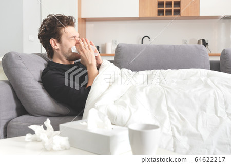 Sick man lying on sofa and blowing nose 64622217