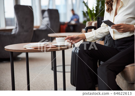 Young woman holding cellphone and grabbing cup of coffee Young woman holding cellphone and grabbing cup of coffee 64622613
