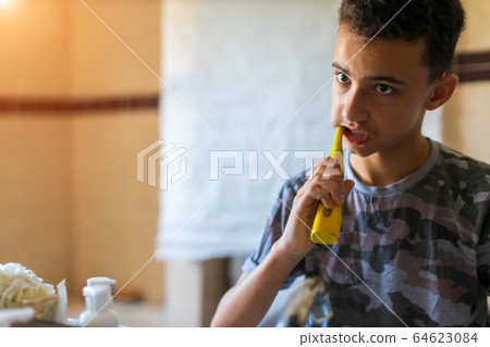 Teenage Boy brushing teeth with electric toothbrush in Bathroom Teenage Boy brushing teeth with electric toothbrush in Bathroom 64623084