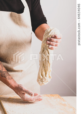 Concept process of making alternative yeast-free home-made bread. A man kneads a kneading pot with dough on the table. Concept process of making alternative yeast-free home-made bread. A man kneads a kneading pot with dough on the table. 64634046