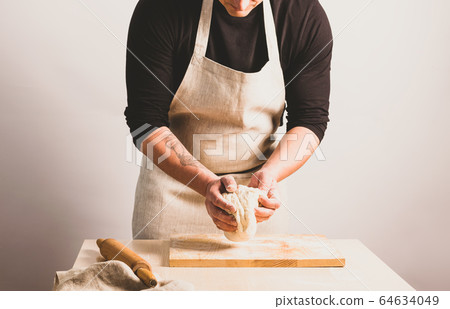 Concept process of making alternative yeast-free home-made bread. A man kneads a kneading pot with dough on the table. Concept process of making alternative yeast-free home-made bread. A man kneads a kneading pot with dough on the table. 64634049