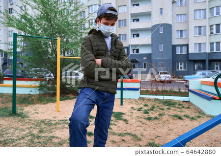 teen boy stands by seesaw on playground near teen boy stands by seesaw on playground near 64642880