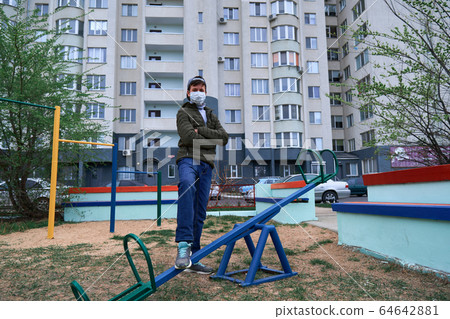 teen boy stands by seesaw on playground near 64642881