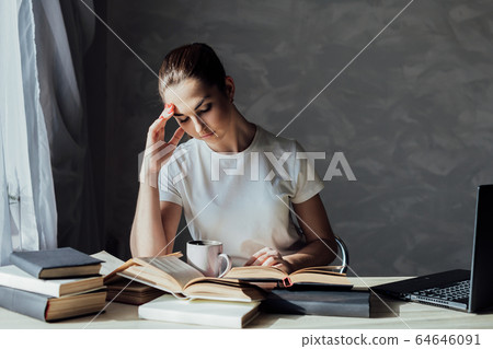 beautiful young woman sitting at a table with books for education and exams 64646091
