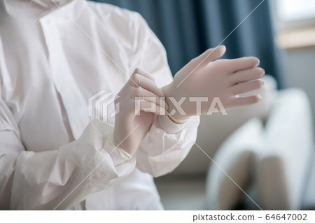 Person in white workwear wearing protective gloves before disinfection 64647002