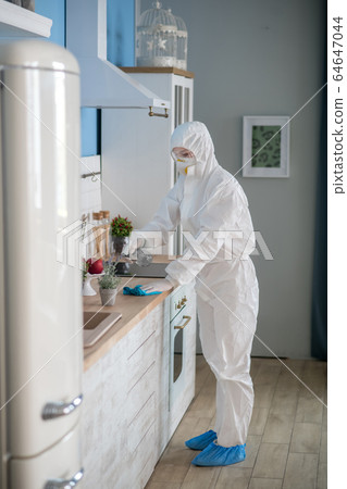 Woman in white workwear and protective eyeglasses disinfecting the surfaces Woman in white workwear and protective eyeglasses disinfecting the surfaces 64647044