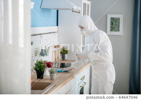 Woman in white workwear and protective eyeglasses disinfecting the kitchen Woman in white workwear and protective eyeglasses disinfecting the kitchen 64647046