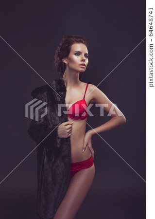 Beautiful sexy long-haired brunette woman in black lingerie and fur coat posing in the studio. The beauty of the face and body. Photos shot in a studio 64648741