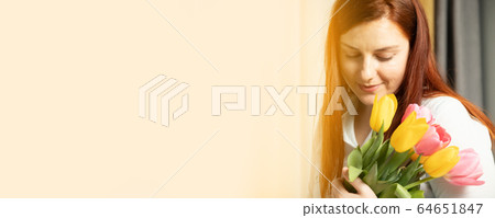 Beautiful cheerful girl with long hair holds a fresh bouquet of tulips on a gray background 64651847