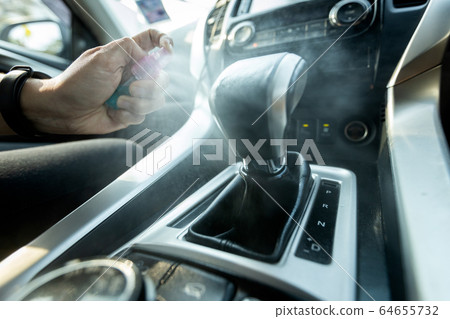 Hand of woman is spraying alcohol,disinfectant spray on gearbox lever in her car,prevent infection of Covid-19,Coronavirus,contamination of germs,bacteria,wipe clean the frequently exposed surfaces 64655732