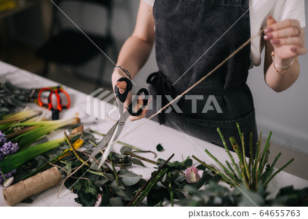 Close-up of hands of woman florist cutting rope for wrapping bouquet of flowers at the table Close-up of hands of woman florist cutting rope for wrapping bouquet of flowers at the table 64655763