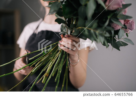 Close-up of hands of woman florist holding bouquet of flowers on white background. Close-up of hands of woman florist holding bouquet of flowers on white background. 64655766