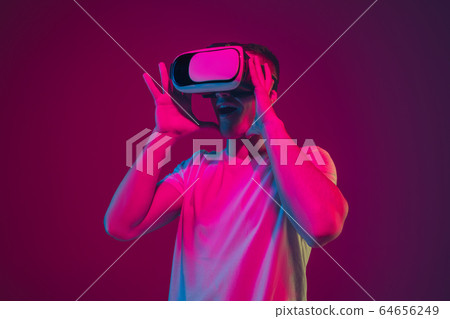 Caucasian man's portrait isolated on pink-purple studio background in neon light, playing with VR-headset 64656249