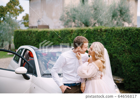Beautiful bride and groom leaning on a convertible and looking at each other in the Medici Villa of Lilliano Wine Estate, Tuscany, Italy. 64656817