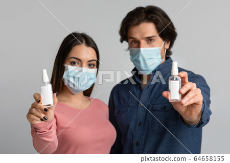 Bottles With Antibacterial Sprays In Hands Of Couple Wearing Medical Masks 64658155
