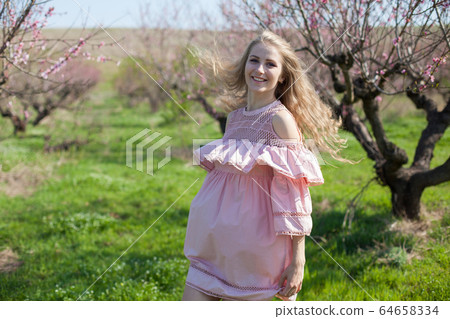 Beautiful blonde woman in pink dress in flowering peach garden in spring Beautiful blonde woman in pink dress in flowering peach garden in spring 64658334