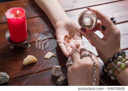 A fortune teller predicts the fate of love with wedding rings, a magic ball, lighted candles and magic stones. A Gypsy woman performs a love spell. A clairvoyant palmist reads by hand with a candle. 64658666