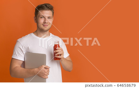 Young man freelancer holding laptop and drinking red healthy detox smoothie Young man freelancer holding laptop and drinking red healthy detox smoothie 64658679