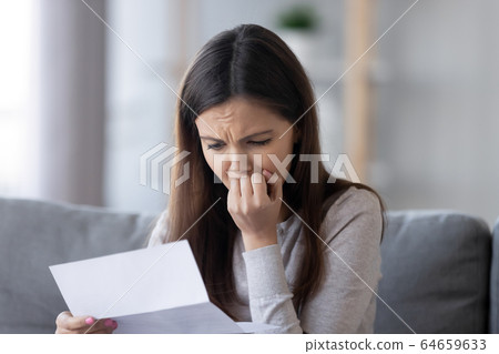 Stressed teen girl feeling worried reading bad news in letter Stressed teen girl feeling worried reading bad news in letter 64659633