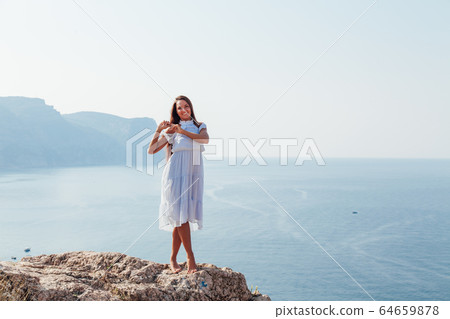 woman in dress looks at the ocean view from the cliff woman in dress looks at the ocean view from the cliff 64659878