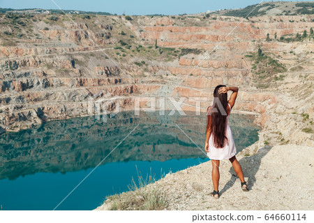 Beautiful woman in dress looks at the view of a mountain lake Beautiful woman in dress looks at the view of a mountain lake 64660114