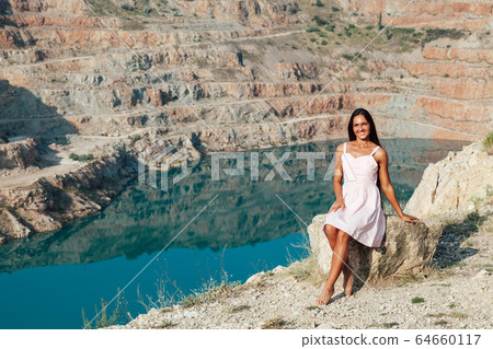 Beautiful woman in dress looks at the view of a mountain lake Beautiful woman in dress looks at the view of a mountain lake 64660117
