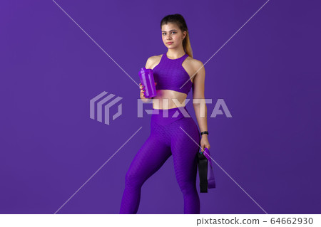 Beautiful young female athlete practicing on purple studio background, monochrome portrait 64662930