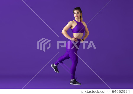 Beautiful young female athlete practicing on purple studio background, monochrome portrait 64662934