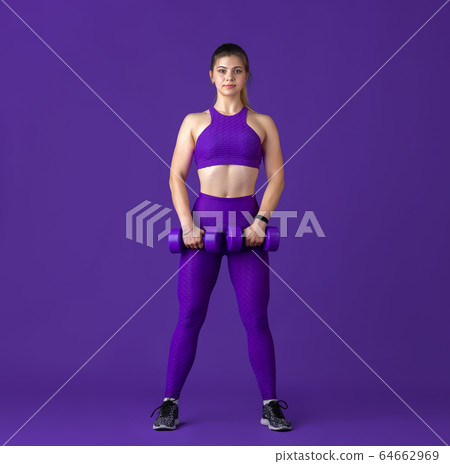Beautiful young female athlete practicing on purple studio background, monochrome portrait 64662969