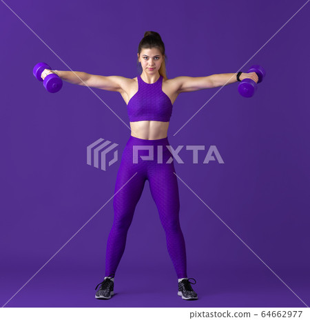 Beautiful young female athlete practicing on purple studio background, monochrome portrait 64662977