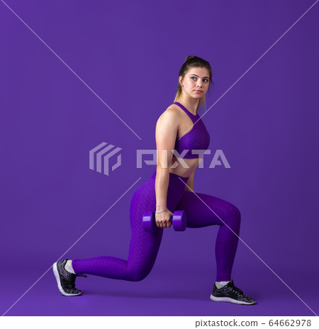 Beautiful young female athlete practicing on purple studio background, monochrome portrait 64662978