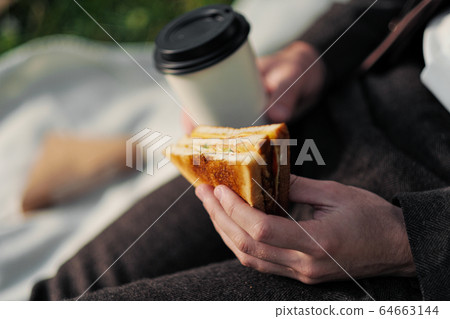 Hands of a man in a suit with a glass of takeaway coffee and a triangular sandwich with tuna. 64663144