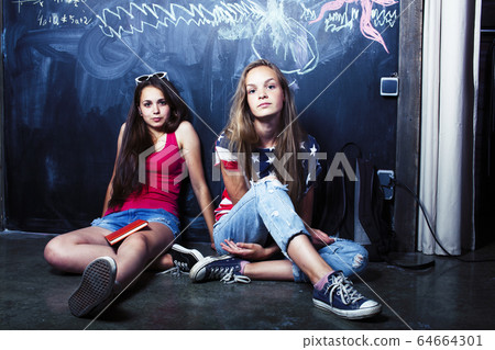 back to school after summer vacations, two teen real girls in classroom with blackboard painted together, lifestyle people concept 64664301